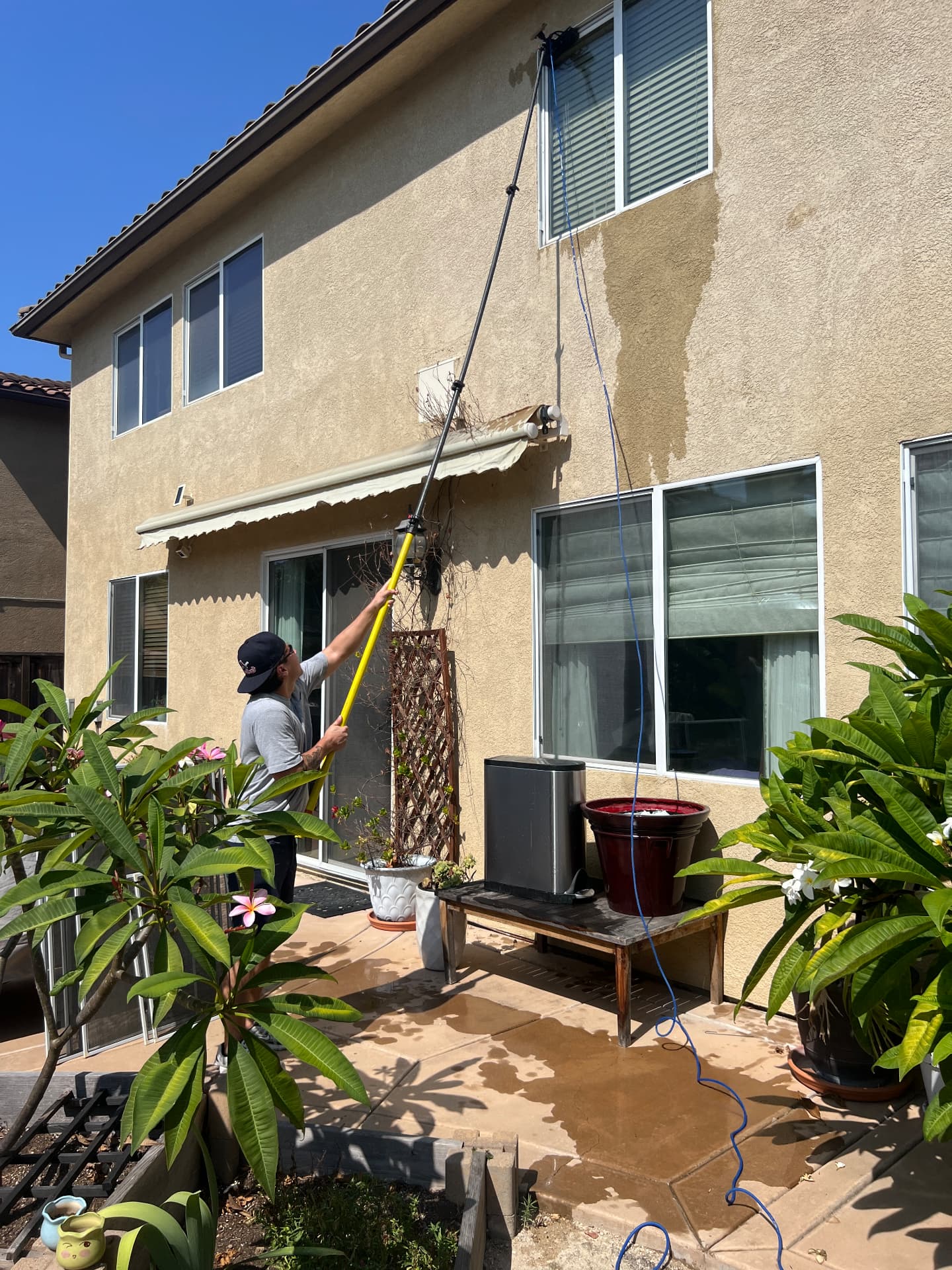 Technician cleaning backyard patio windows on a stucco home
