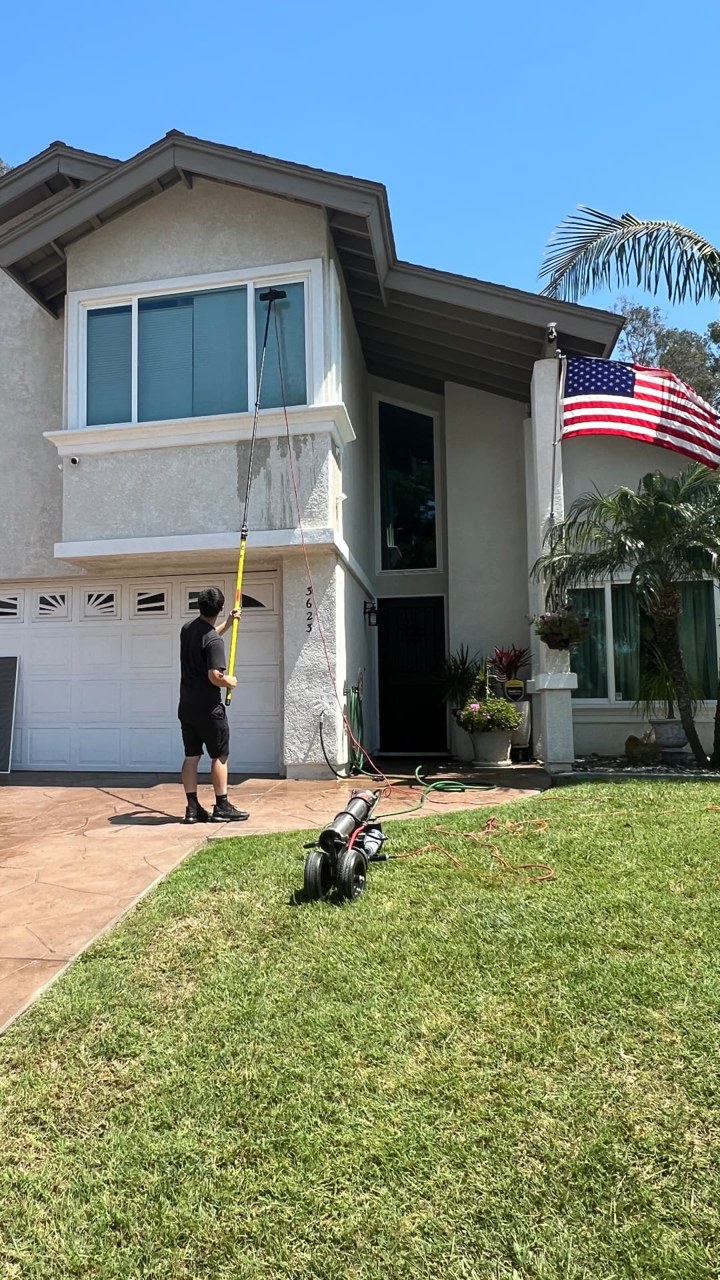 ClearView technician cleaning a two-story home's upper windows with a water-fed extension pole