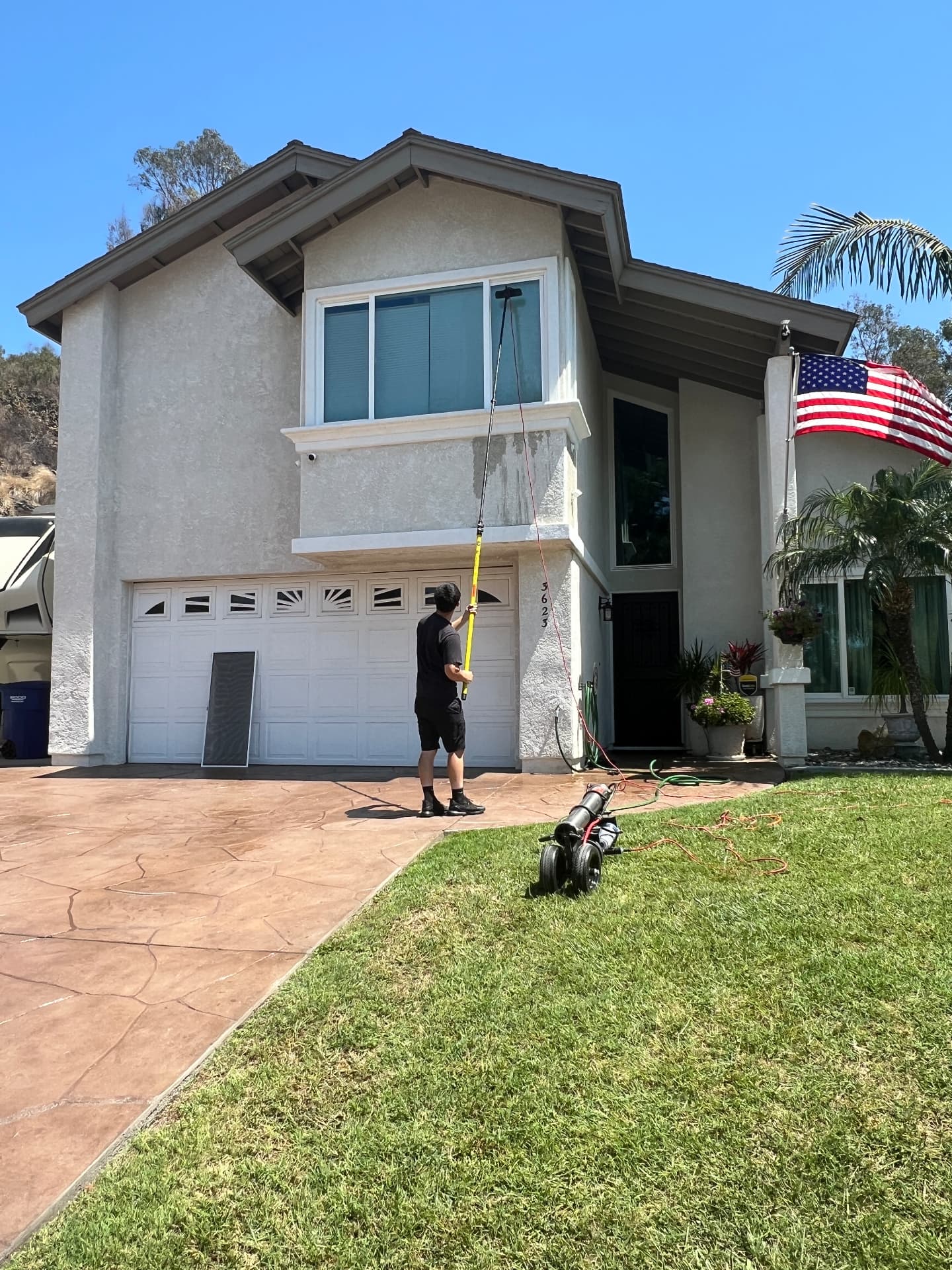 Technician cleaning a two-story home's upper windows with a water-fed pole